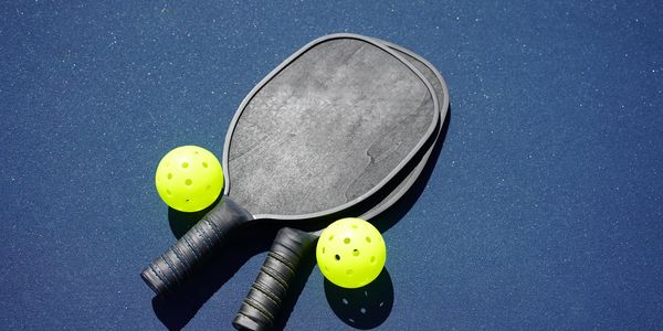 Two pickleball paddles and two yellow balls on a blue surface.