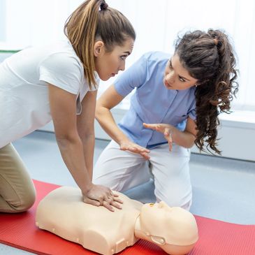 A woman receives CPR training on a mannequin from an instructor.
