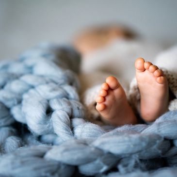 Close-up of baby feet peeking out from a chunky blue knit blanket.