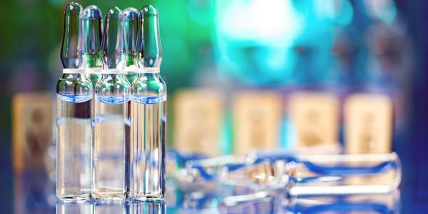 Glass ampoules filled with clear liquid on a reflective surface.