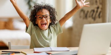 Excited child raising arms in front of laptop.