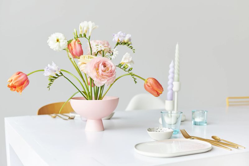 A modern spring bouquet with freesias, ranunculus and tulips in a beautiful vase on a white dining table