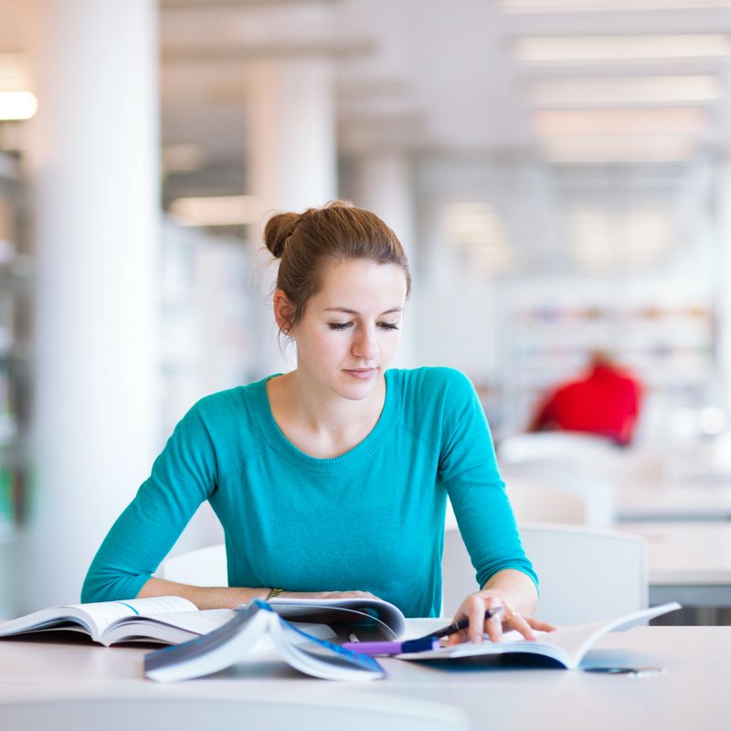pretty female college student studying in a high school/college library (shallow DOF; color toned image)