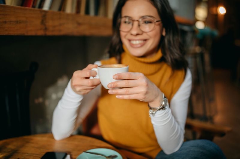 Beautiful  women in casual clothes is smelling coffee and smiling while resting in cafe