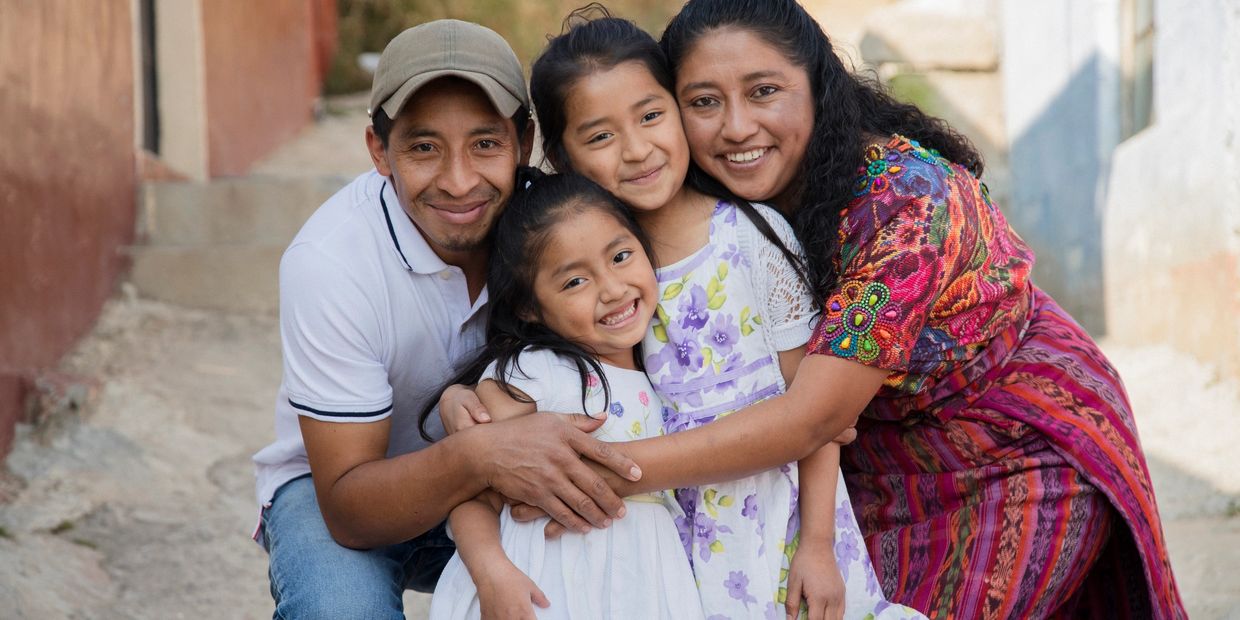 A happy family of four smiling and hugging outdoors.