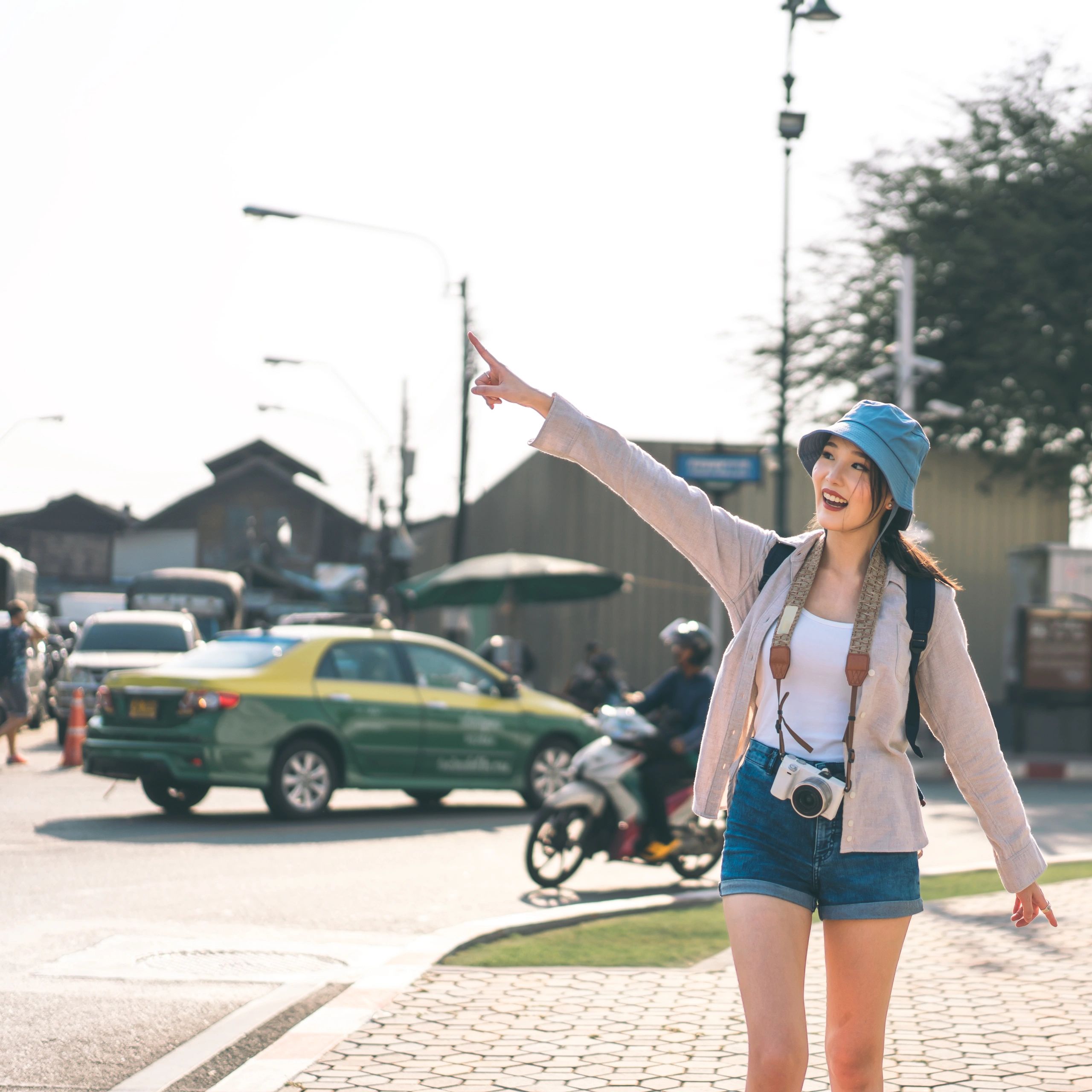 Woman in blue bucket hat happily pointing with camera around her neck.