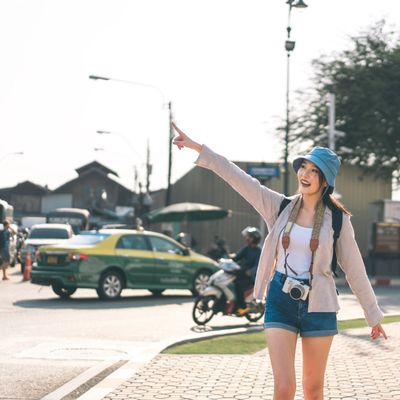 Young woman hailing a taxi on a sunny city street, smiling and wearing casual summer clothes.