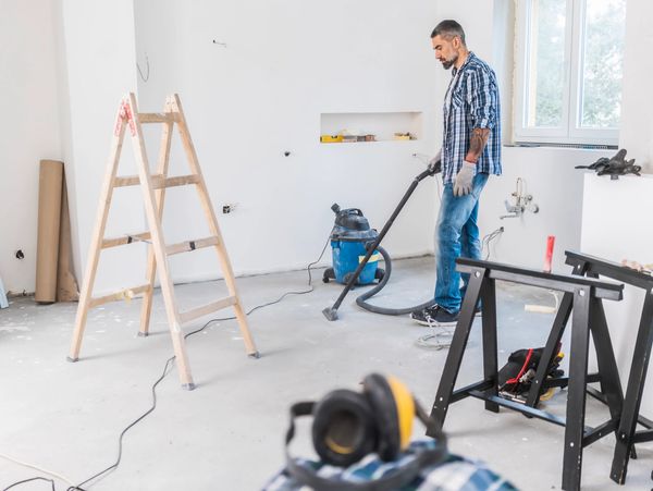 Man vacuuming floor in a room under renovation.