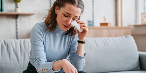 Woman crying and wiping tears with tissue on couch.