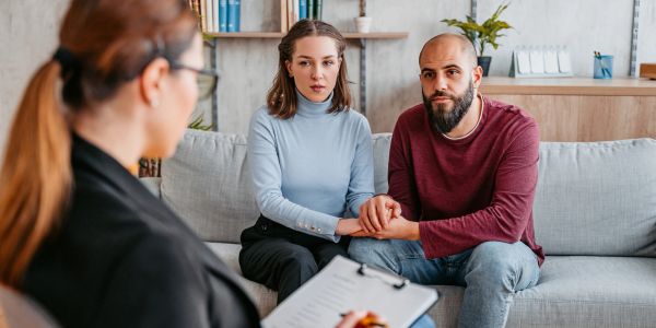 Couple holding hands during therapy session with counselor.