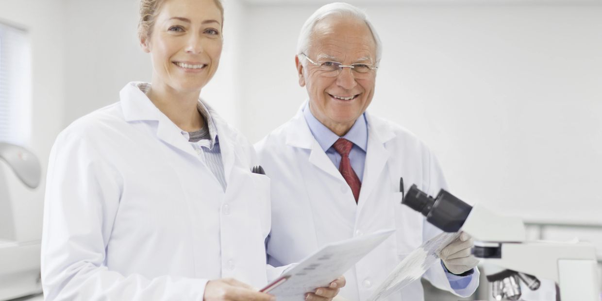 Two scientists in lab coats smiling in a laboratory with a microscope.