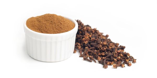 Ground cloves in a white bowl with whole cloves nearby.