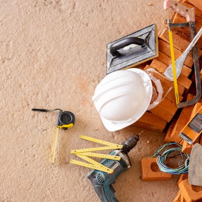 Construction tools including a hard hat and drill on bricks.