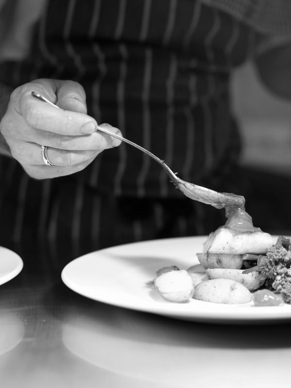 Chef plating gourmet dish with sauce.