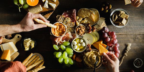 Charcuterie board with hands reaching for snacks.