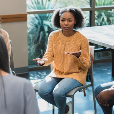 Woman in a yellow sweater speaking in a group setting.
