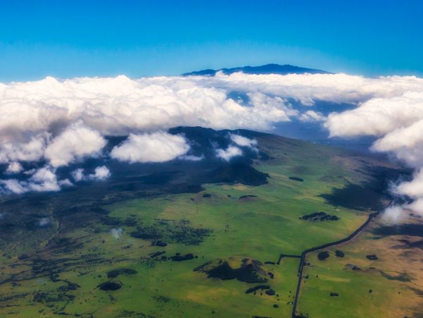 Aerial view of green hills with clouds and blue sky above.