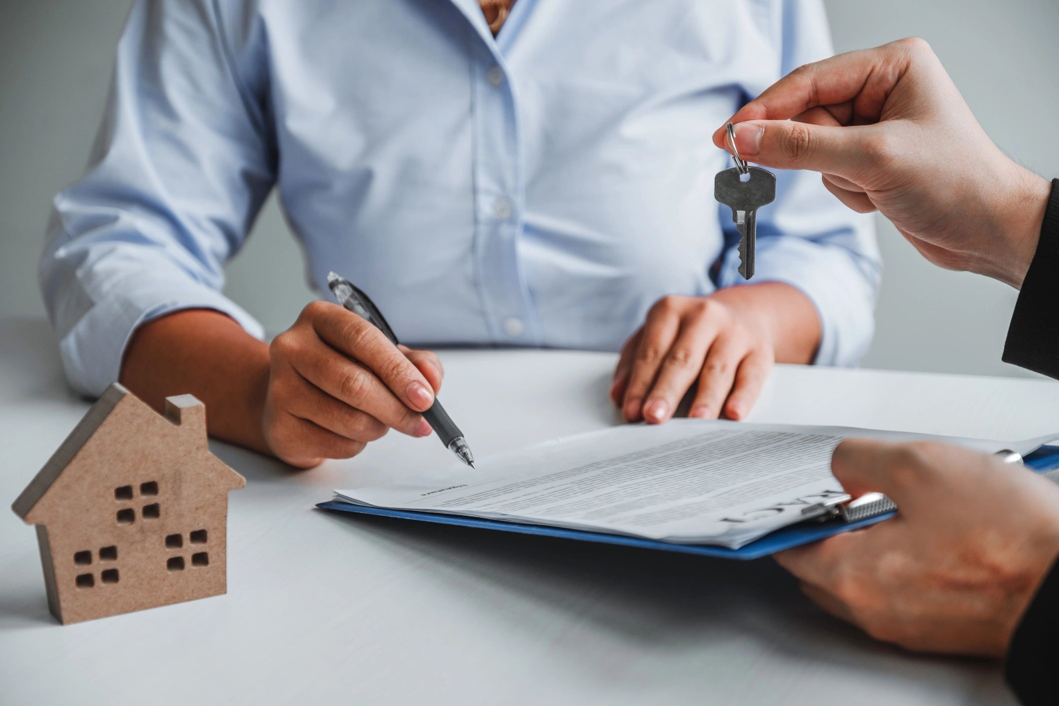 Business people signing loan agreement documents on desk with calculator, pen and small house model 