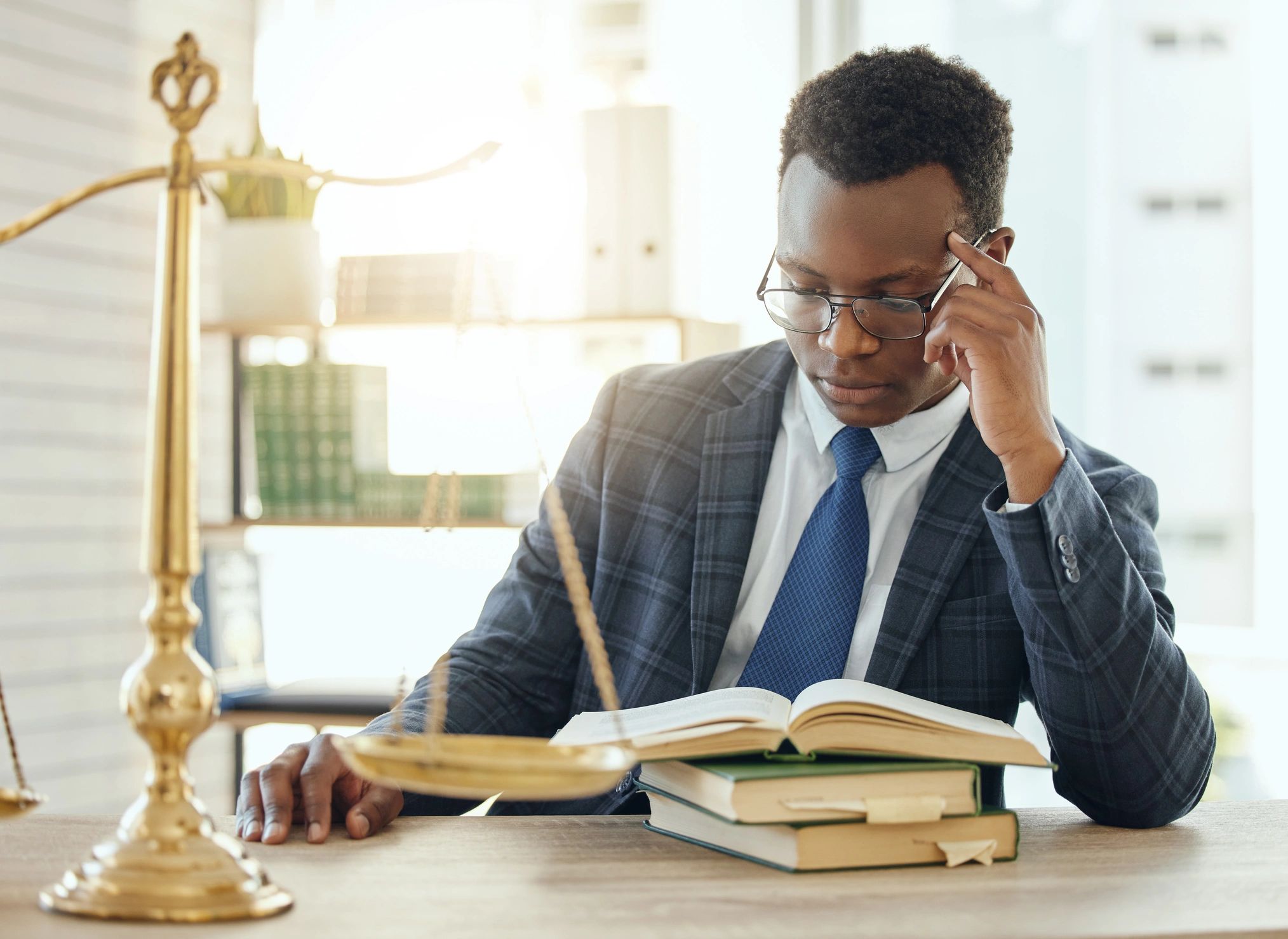 Man in suit reading books with a scale of justice beside him (paralegal studying).