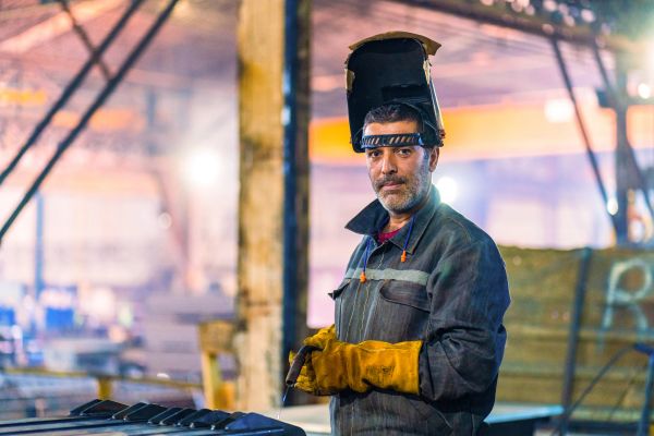 Welder in protective gear holding a welding tool in a workshop.