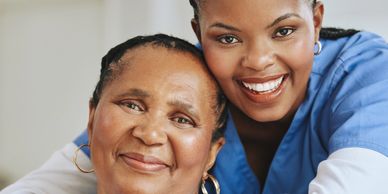 A smiling nurse in blue scrubs embraces an elderly woman with warmth and care.