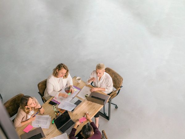 Four women collaborating around a table with laptops and documents.