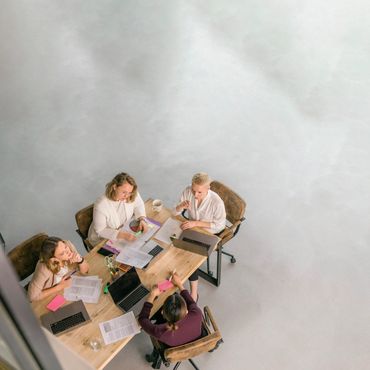 Four people discussing work around a table with laptops and documents.