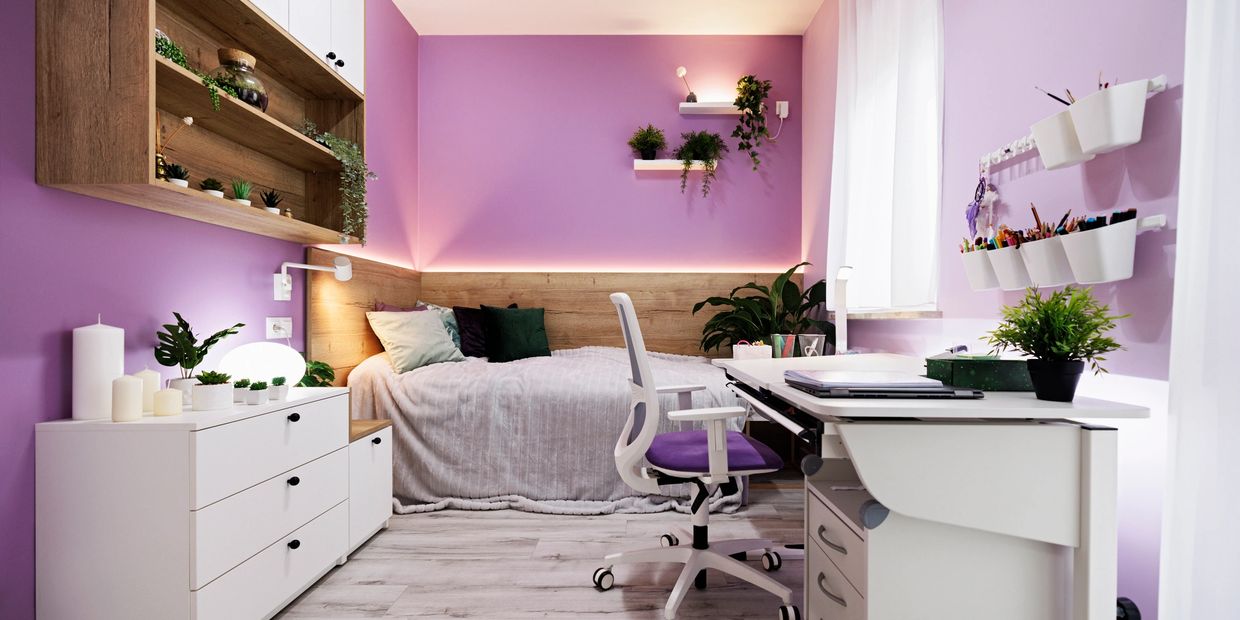Cozy purple-themed bedroom with a work desk and decorative plants.