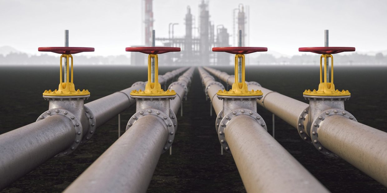 Four large industrial pipelines with red and yellow valves leading to a refinery.