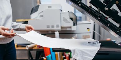 Person holding printed cloth near a heat press machine.
