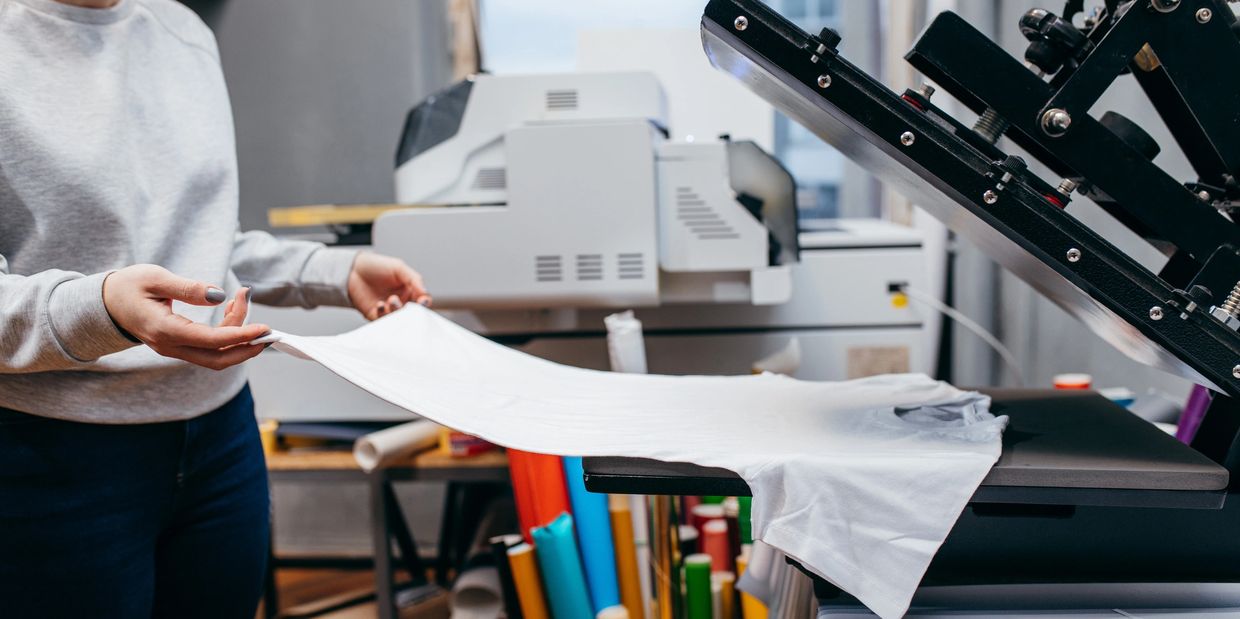 Person placing a white t-shirt on a heat press machine.