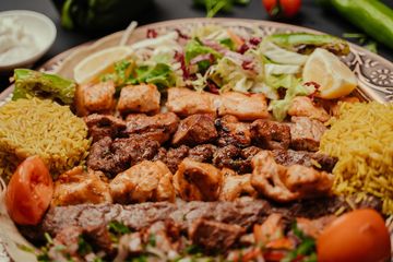 A platter with grilled meat, yellow rice, salad, and lemon wedges.