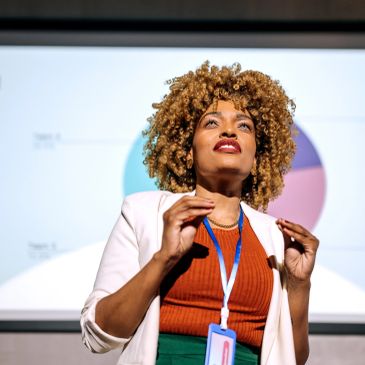 Woman speaking confidently with a presentation behind her.