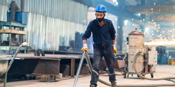 Factory worker with safety gear handling equipment in an industrial setting.
