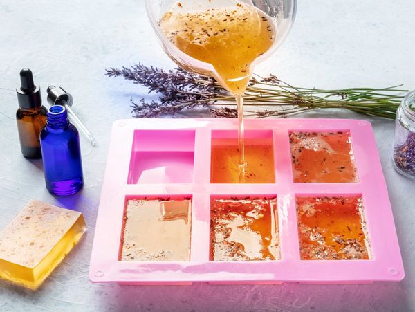 Pouring liquid soap mixture with lavender into silicone molds for homemade soap.