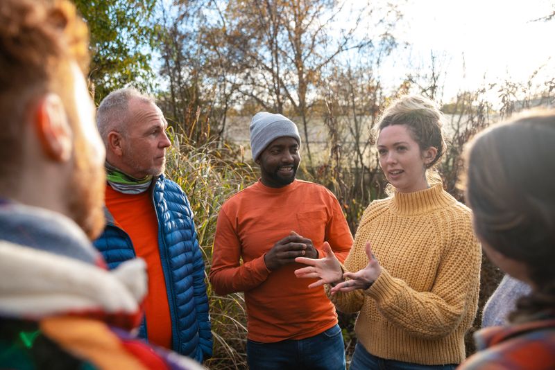 A multiracial group of volunteers wearing warm casual clothing and accessories on a sunny cold winters day. They are talking before they start working on a community farm, planting trees and performing other tasks.