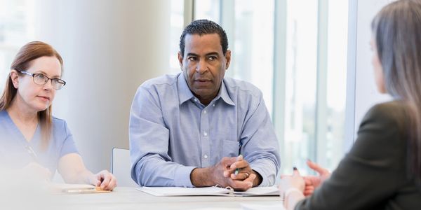 Three professionals engaged in a serious meeting around a table in a bright office.