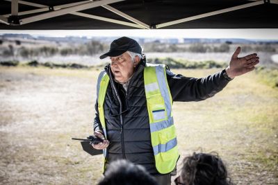 Man in high-visibility vest speaking outdoors with a mobile device.