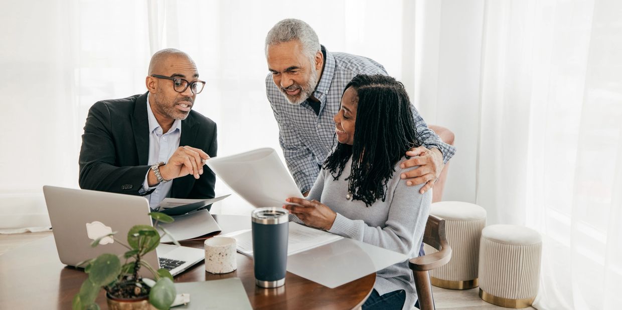 Couple discussing documents with a financial advisor at a wooden table.
