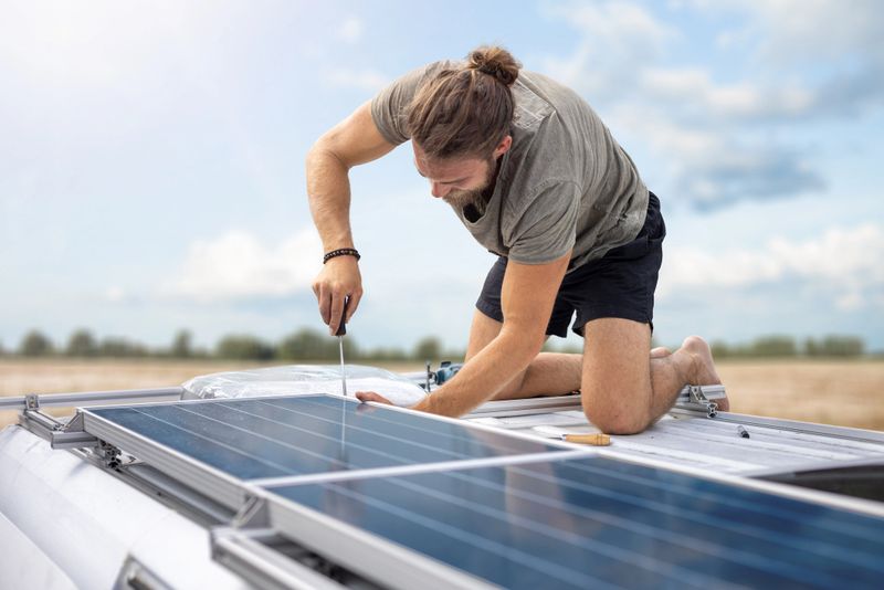 Man installing solar panels on top of the roof of a camper van.