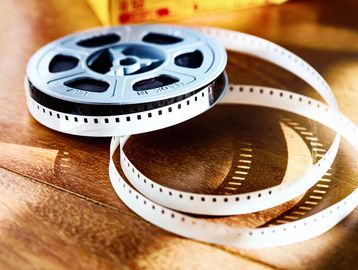 A close-up of 8mm film reel with unspooled film strip on a wooden surface.