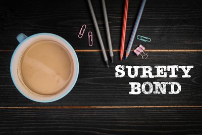 A cup of coffee with colored pencils and the text 'SURETY BOND'.