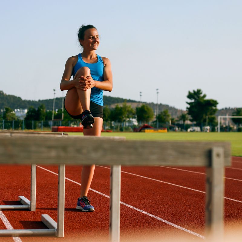 Young woman stretching before exercising on track. About 20 years old, Caucasian female.