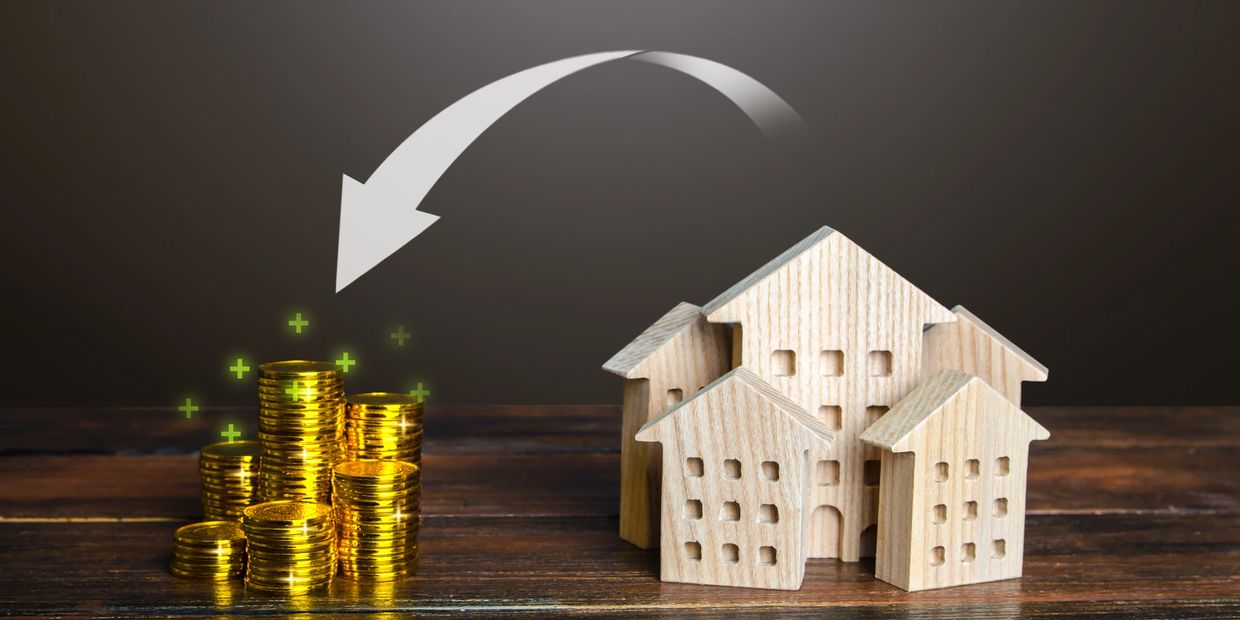 Stacked coins with an arrow pointing to wooden house models, symbolizing investment in real estate.