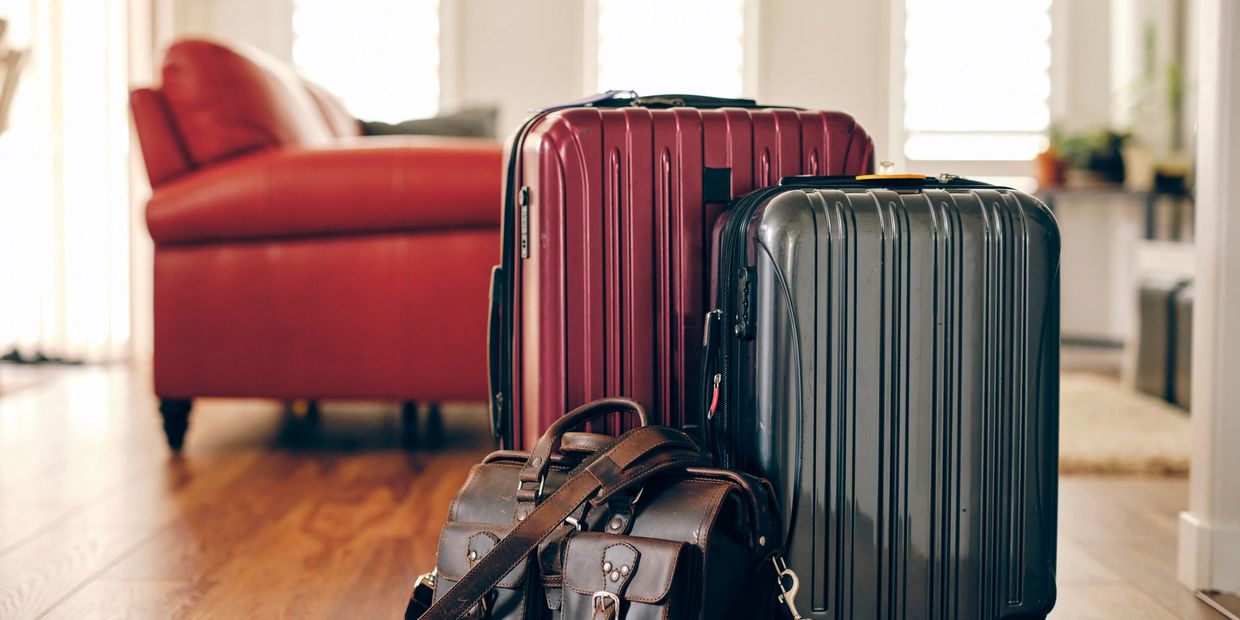 Packed suitcases and bags near a red sofa inside a house.