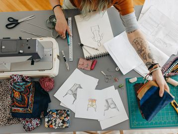 Designer working on fashion sketches at a cluttered table.