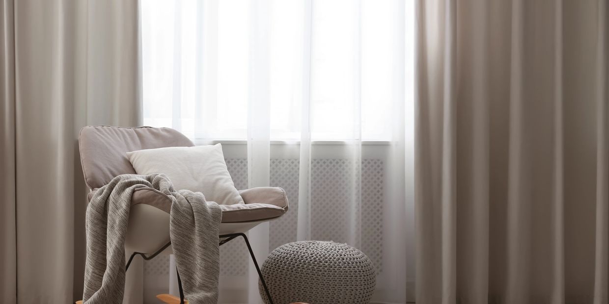 Cozy rocking chair with blanket and pillow beside a knitted pouf in a softly lit room.