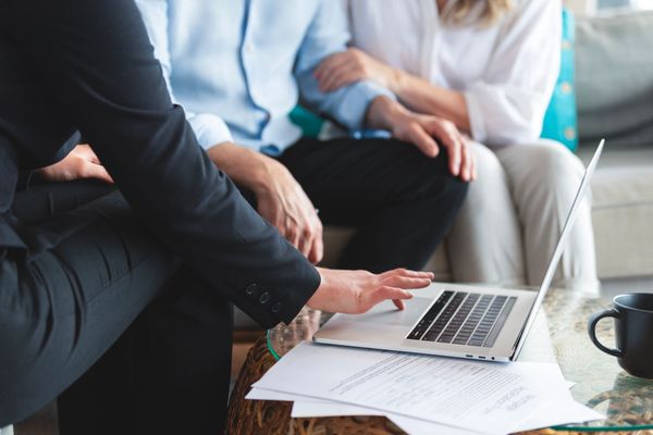 People discussing documents with a laptop on a table.