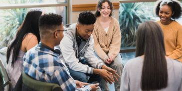 A group of young adults sitting in a circle, engaging in a friendly discussion.