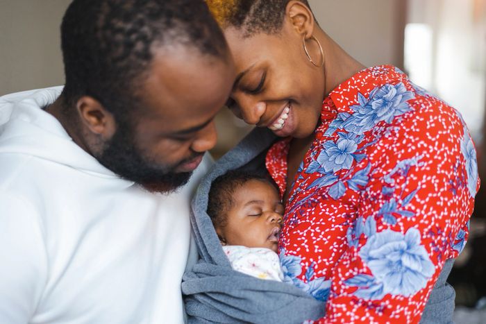 Parents lovingly embrace their sleeping baby wrapped in a cozy blanket.